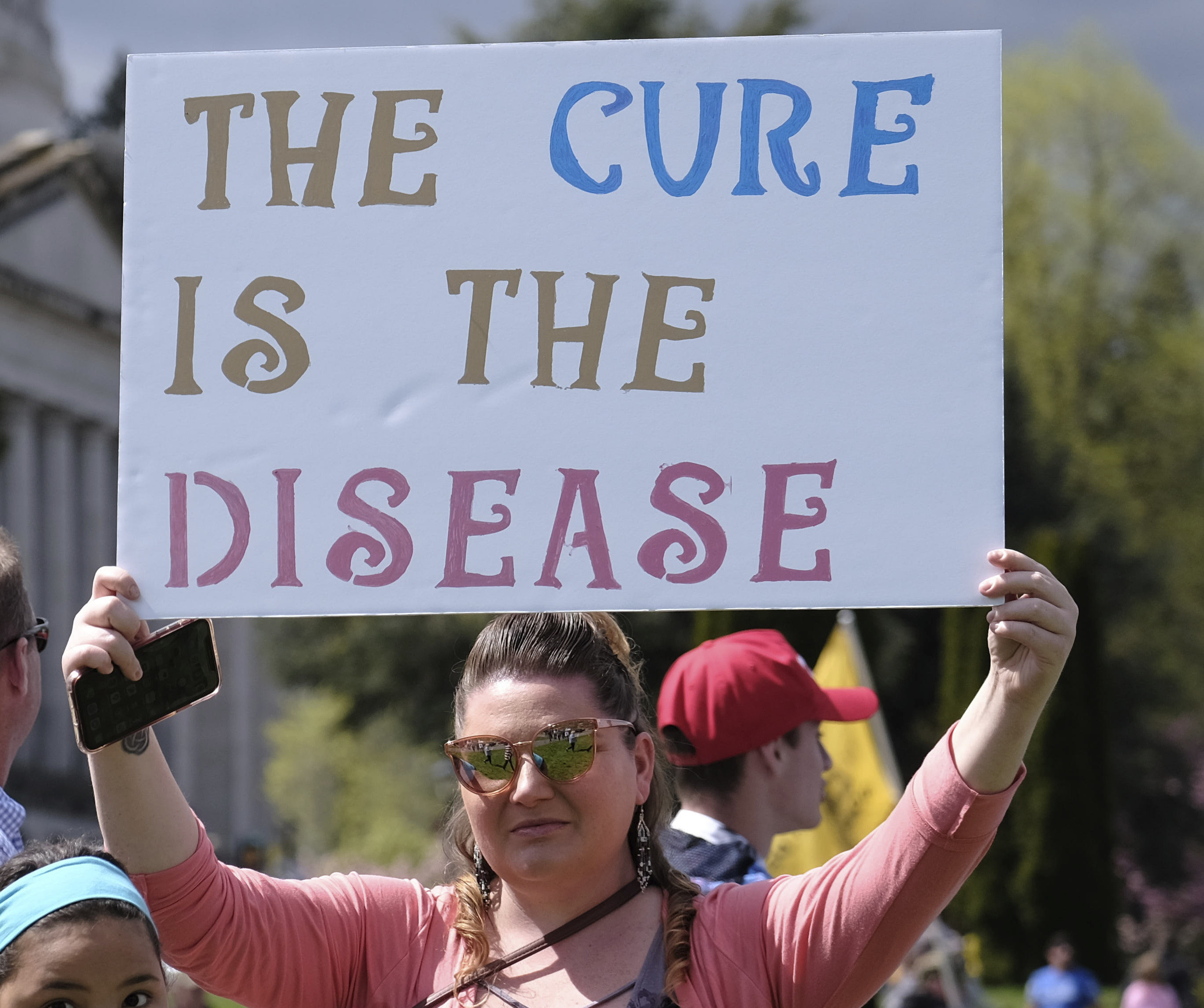Woman holding up a sign reading, &quot;The cure is the disease&quot;