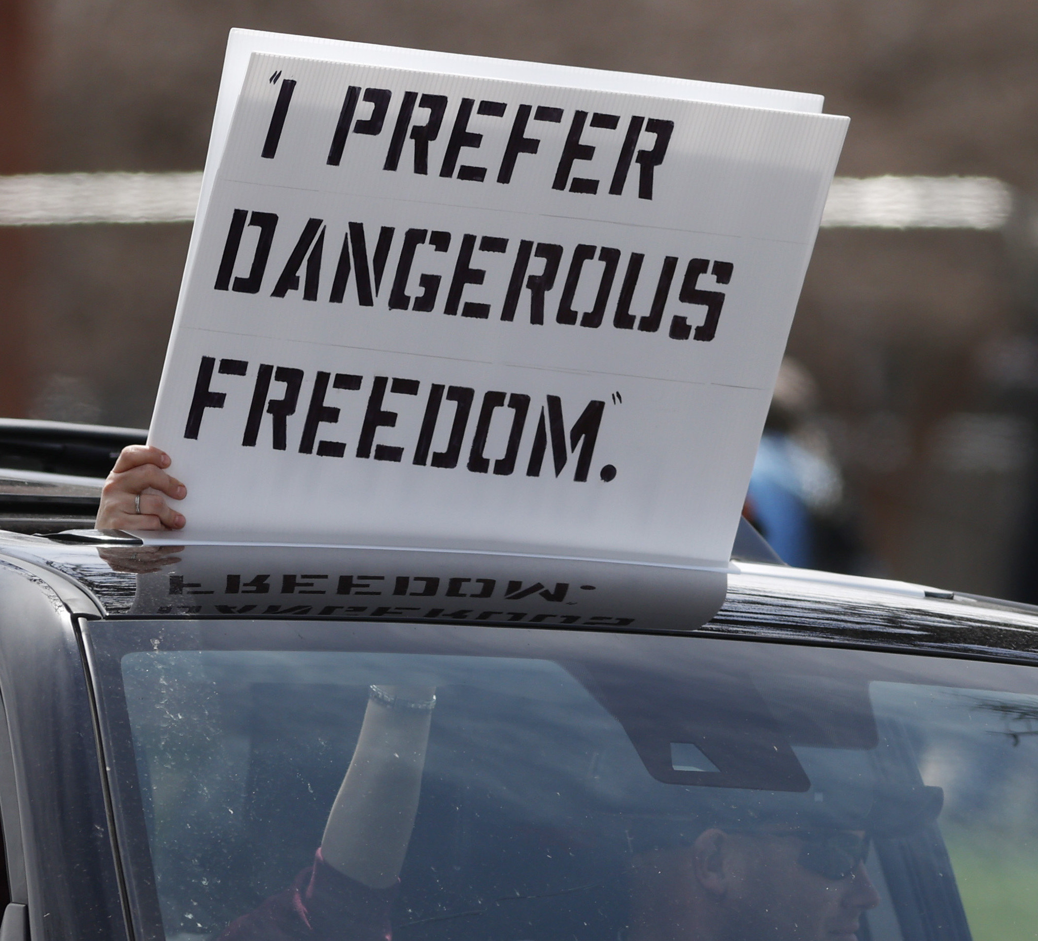 Person in a car with a sign reading, &quot;I prefer dangerous freedom&quot;
