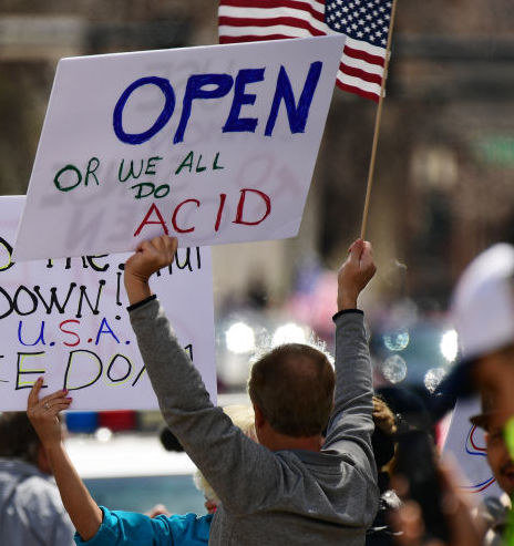 Man holding a US flag and a sign reading, &quot;Open or we all do acid&quot;