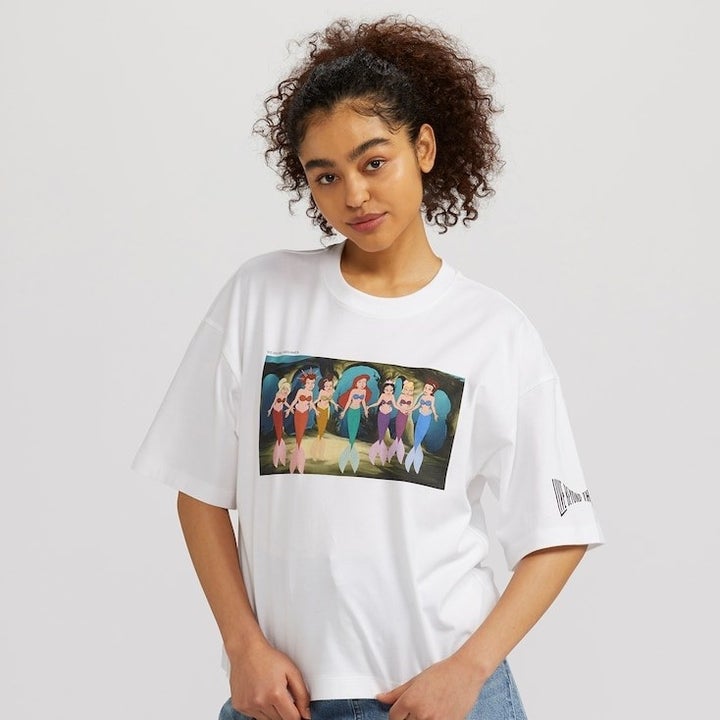 a model wearing an oversized white tee with a graphic of ariel and all of her sisters
