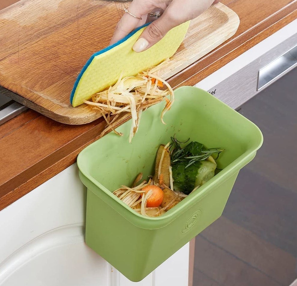 Small bin in green attached to a counter with food scrape inside of it