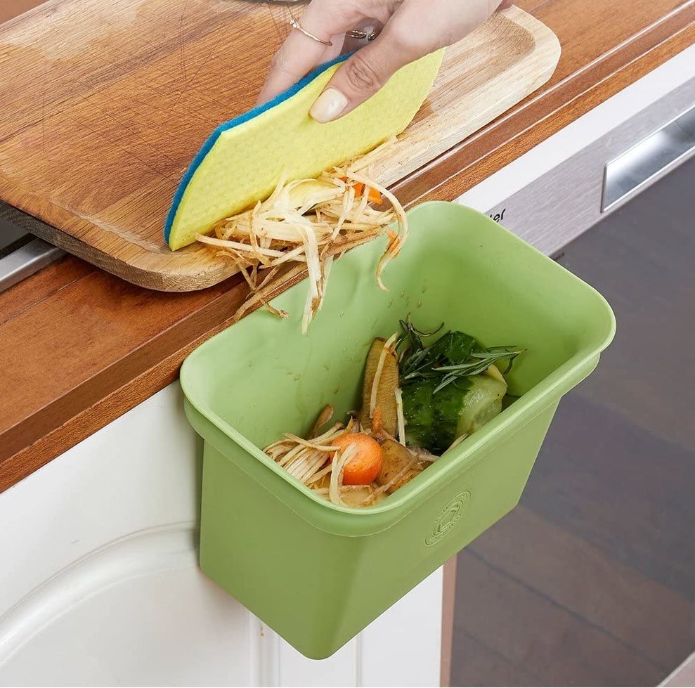 Small bin in green attached to a counter with food scrape inside of it