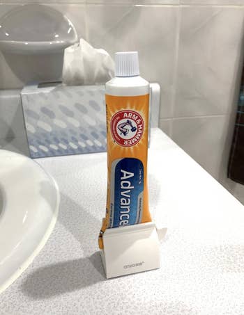 reviewer image of the white holder on a bathroom counter with a tube of toothpaste rolled into it