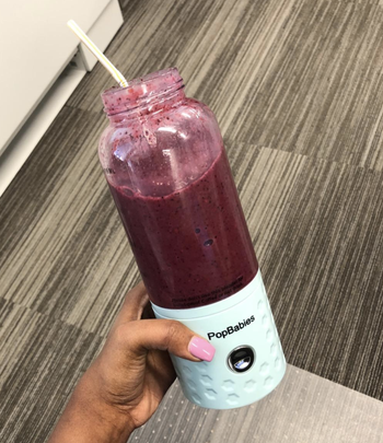 reviewer holding blender with light blue base and purple smoothie inside 