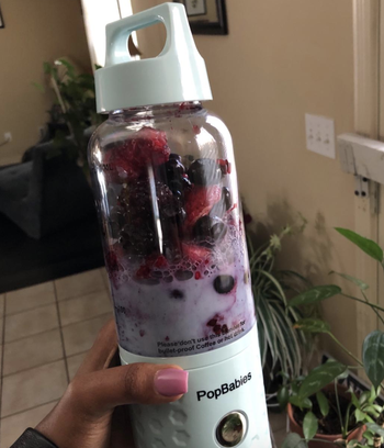 reviewer holding the same blender with strawberries and blueberries inside 