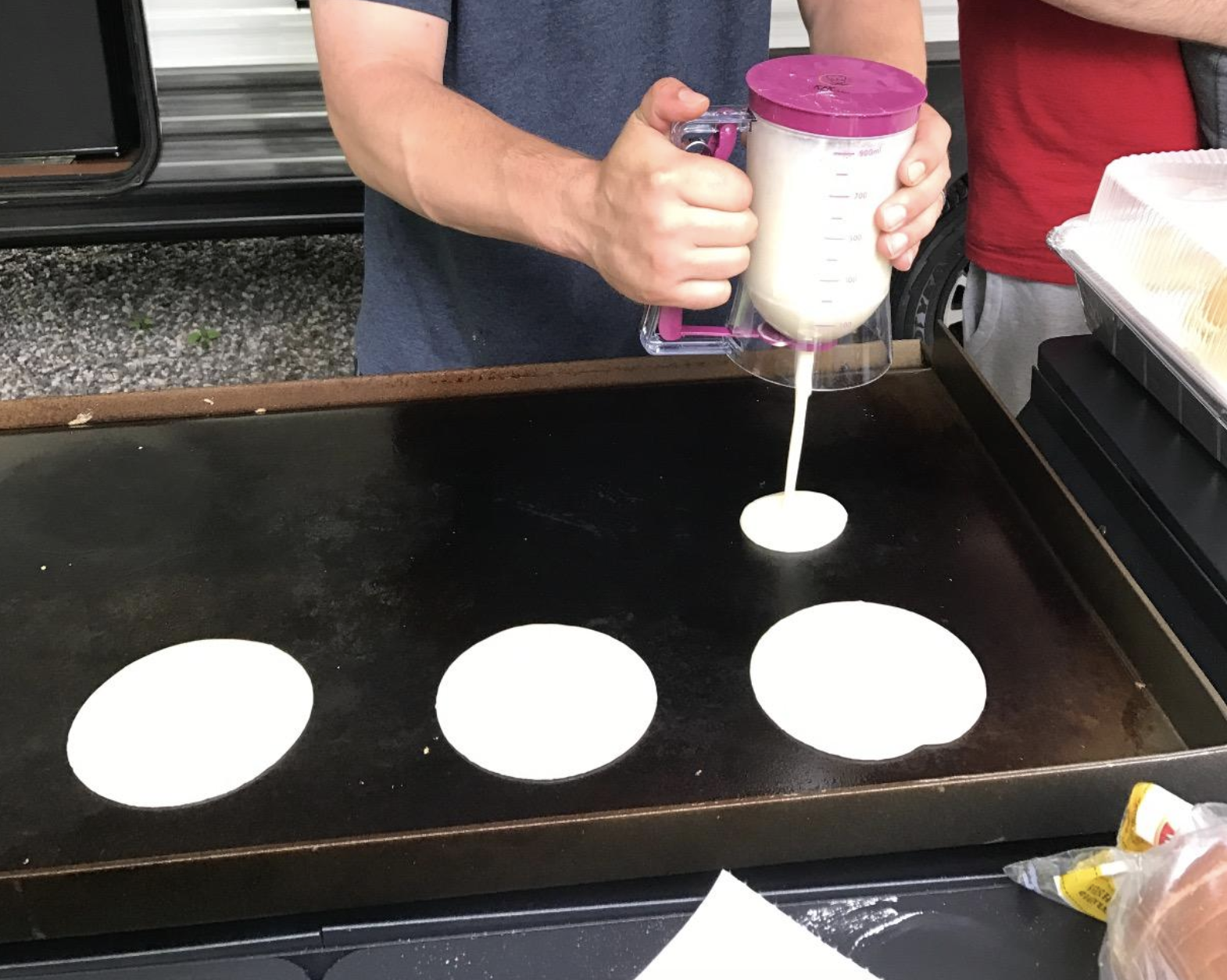 Model holding the circular batter dispenser and pouring out pancake batter on to a griddle