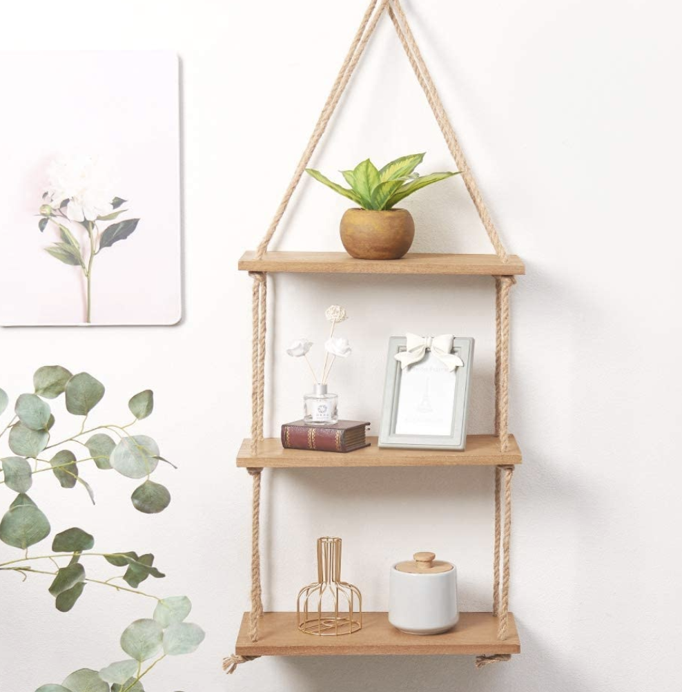 A hanging shelf filled with a tiny plant and gold sculptures on a wall
