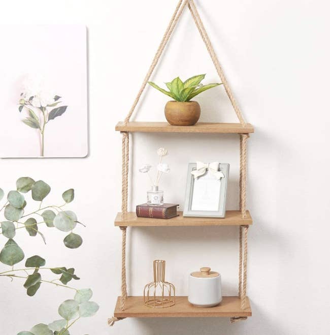A three-tier hanging shelf filled with a tiny plant and gold sculptures on a wall
