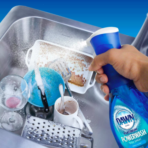 person spraying the spray onto the contents of a kitchen sink with dirty dishes