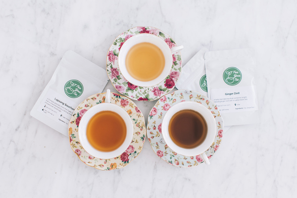 three different colored teas in teacups on top of pretty floral saucers