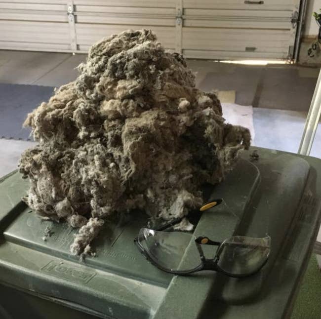 Pile of dryer lint connected apical of a garbage can, with information glasses resting nearby