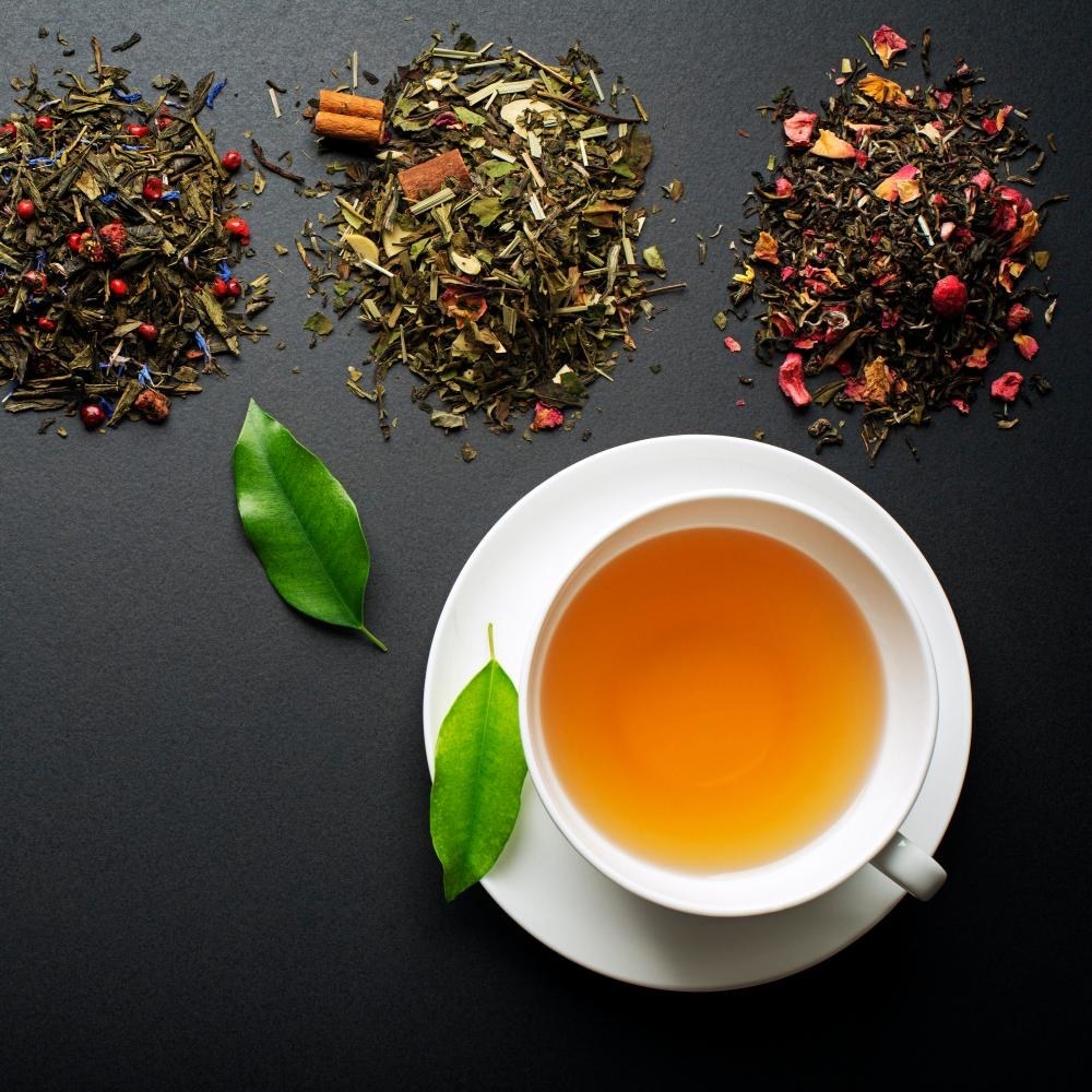 a white tea-filled cup below three piles of different loose tea leaves