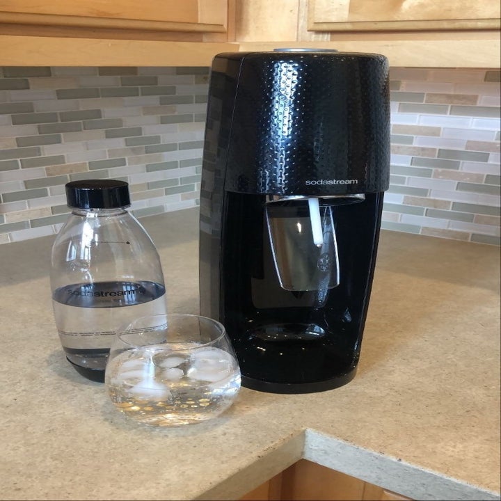 the black sodastream next to a glass and a bottle