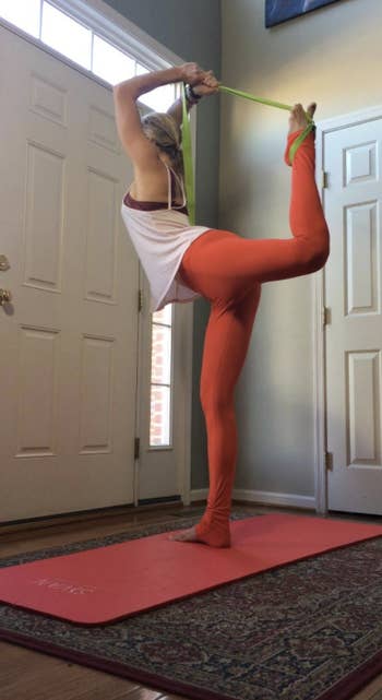 reviewer uses lime green yoga strap to stretch leg in yoga pose