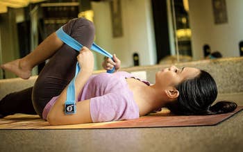 model lies on the floor to stretch with blue yoga strap