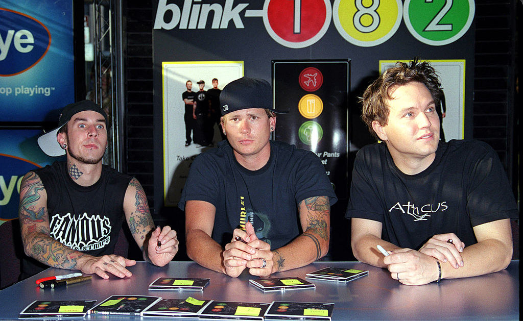 A photo of Blink-182 sitting down signing copies of their album &quot;Take Off Your Pants and Jacket&quot;