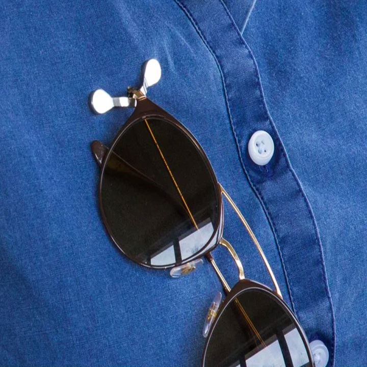 the curved metal hook on a person's shirt kind of like a brooch or pink. A pair of sunglasses are hanging from it.