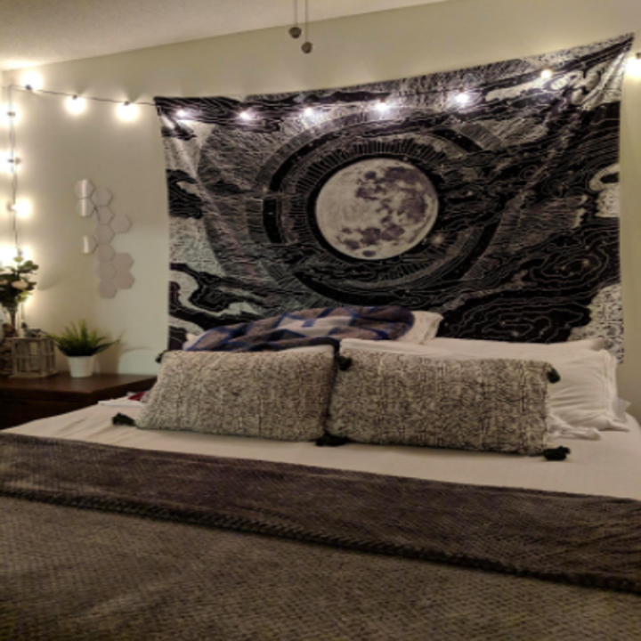 reviewer's pic of a bed with a black moon motif tapestry hung on the wall in place of a headboard
