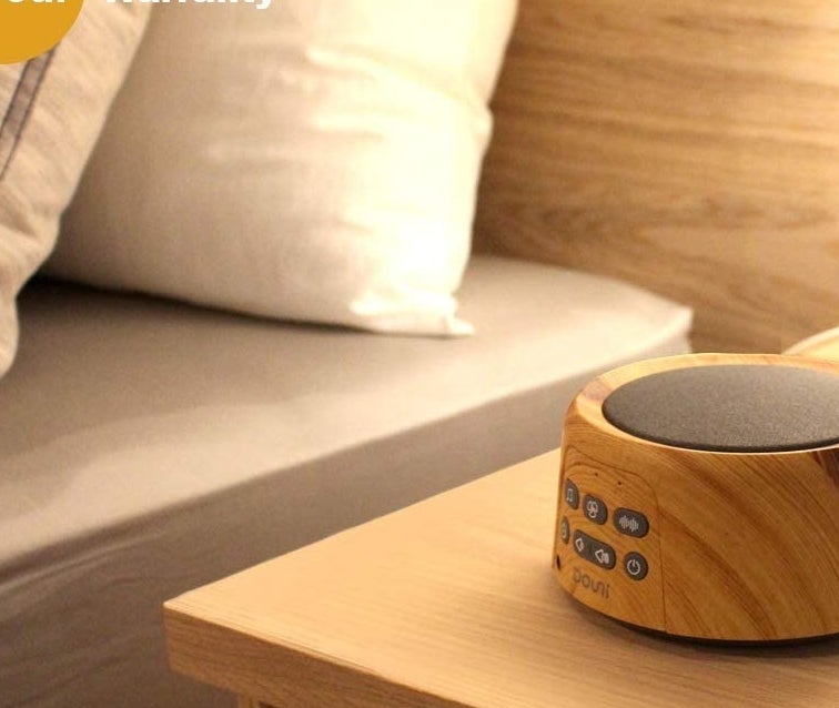 A circular white noise machine with a wooden finish and a gray speaker on top