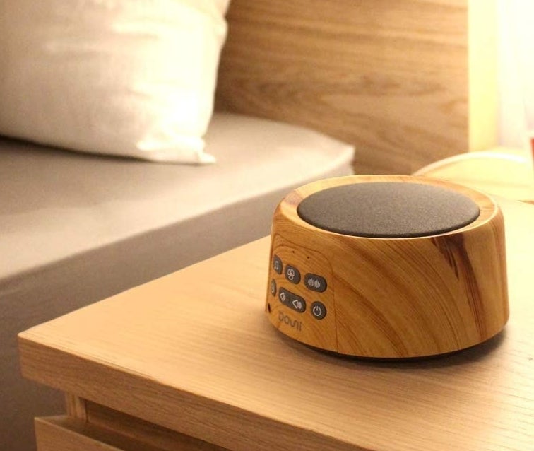 A circular white noise machine with a wooden finish and a gray speaker on top