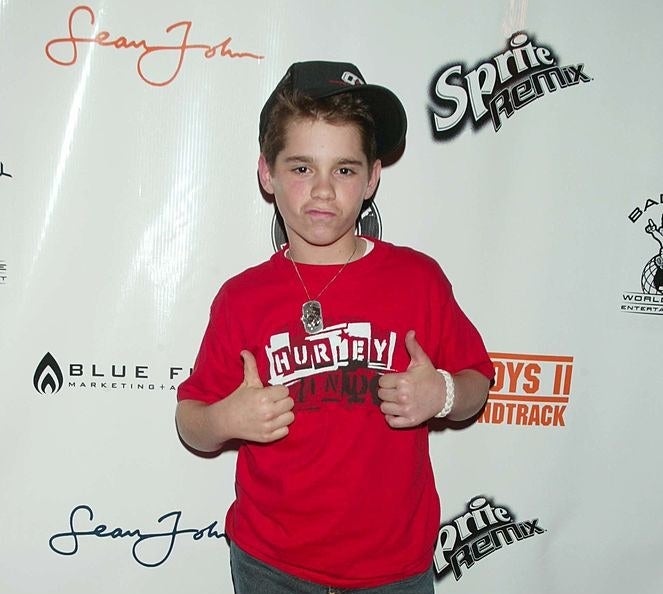 Ryan Pinkston on the red carpet of the event wearing a red Hurley tee, dog tags, and a baseball cap to the side.