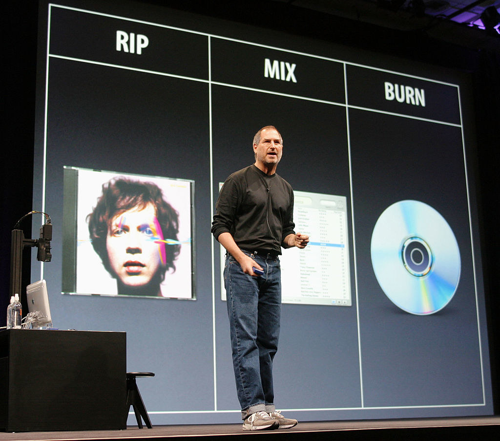 Steve Jobs during an Apple presentation with RIP featuring a Beck CD, and then the  words burn showing iTunes, and then burn showing a plain CD.