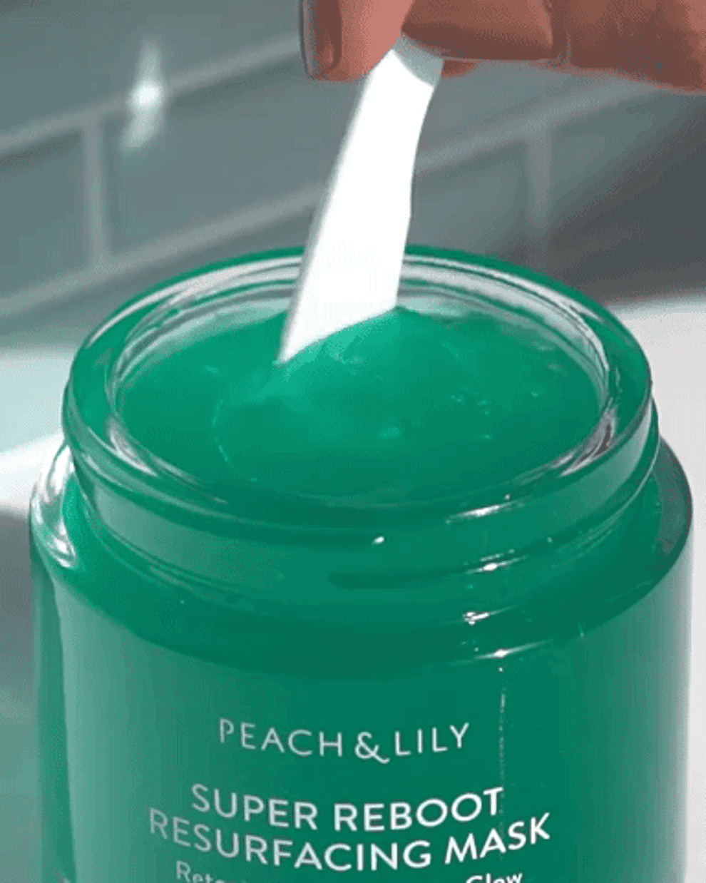 a hand stirs the green jelly-like masks with a tiny plastic applicator 