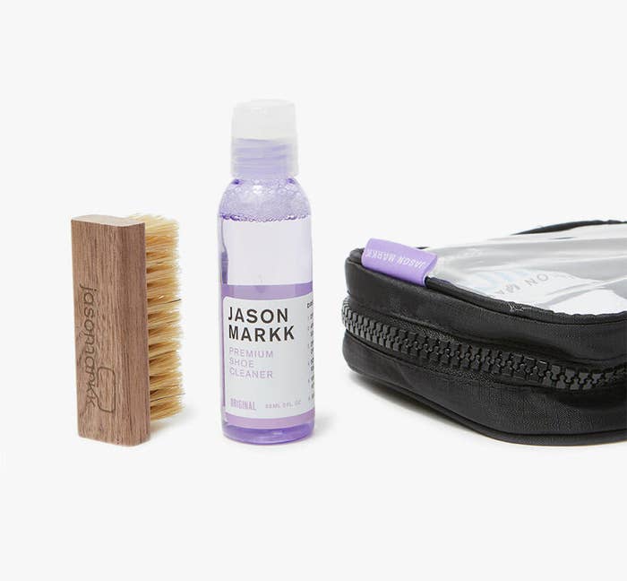 Purple cleaner bottle filled with clear solution next to brush and bag 