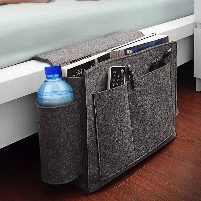 A bedside caddy storing a water bottle, remote and other miscellaneous items.