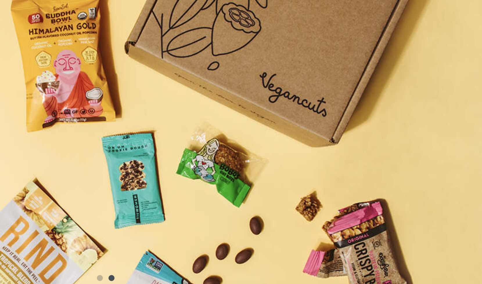 A Vegan cuts subscription box next to assorted vegan popcorn and snack bars