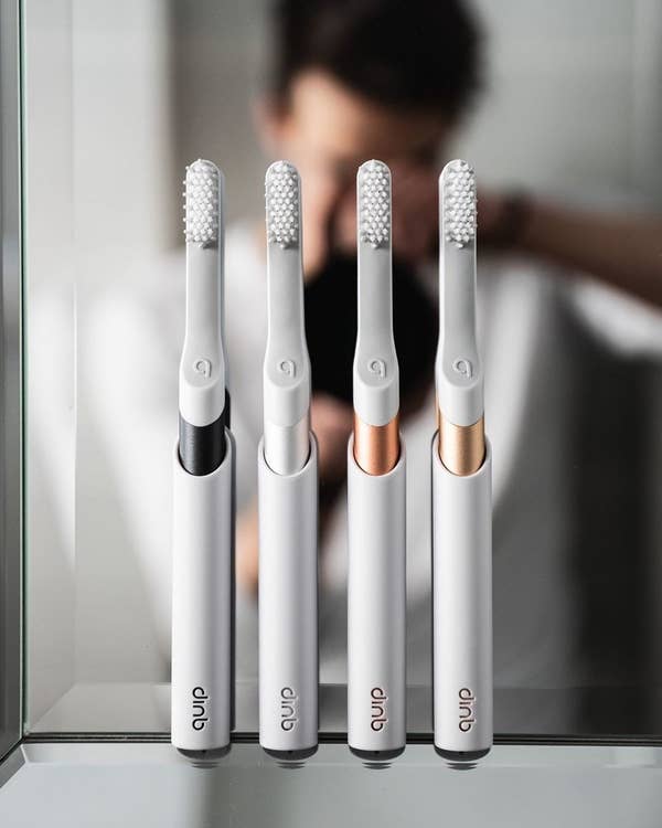 four metallic quip toothbrushes stuck to a mirror in their holders