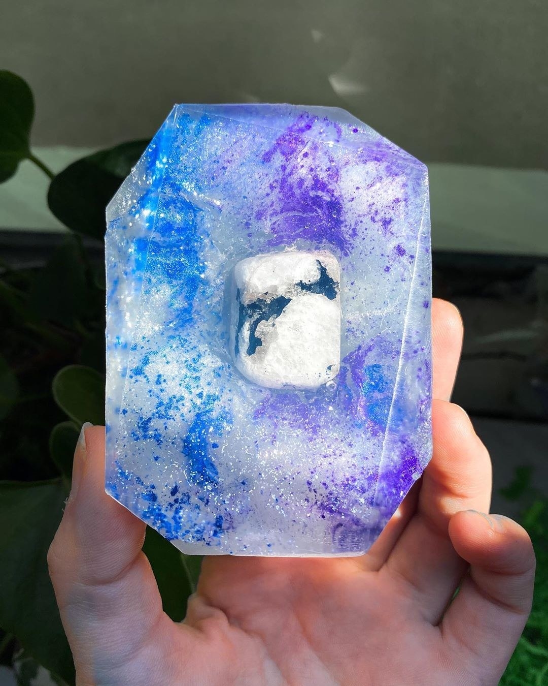 a clear bar of soap with purple and blue sparkles throughout and a crystal stone in the mdidle