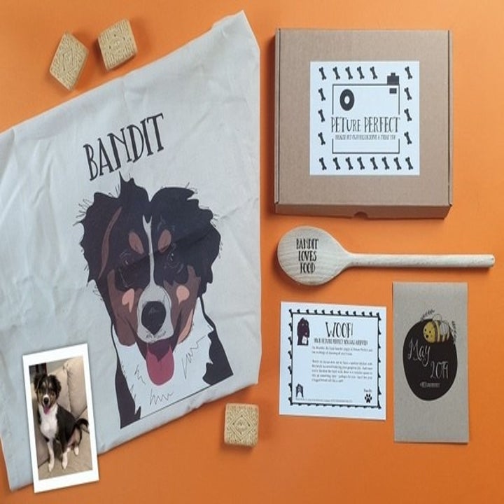 flatlay of a "Peture Perfect box" with a picture of a dog an illustration od the dog on a towel reading "bandit" and a wooden spoon with "bandit loves food" carved into it