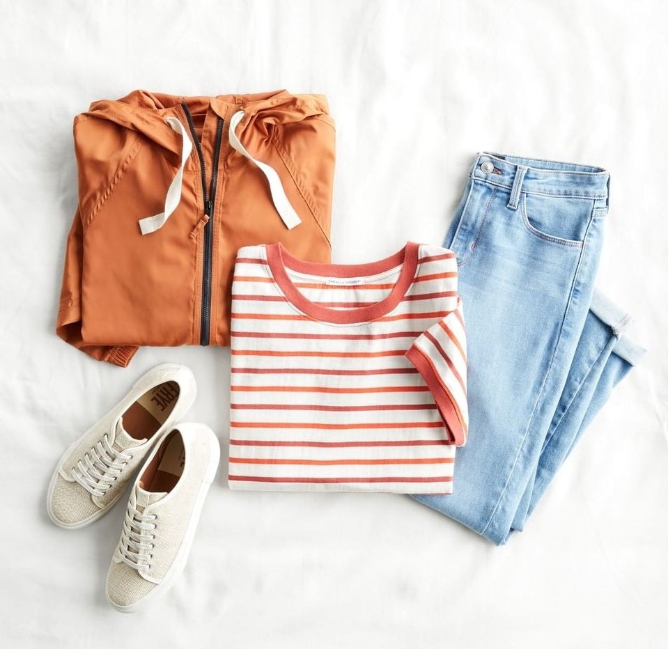 flatlay with an orange hoodie, striped tee, jeans, and white sneakers. 