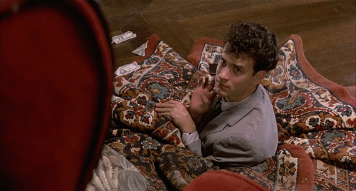 Tom Hanks waving as he's stuck in a carpet that has fallen into a hole in a hardwood floor from the film The Money Pit