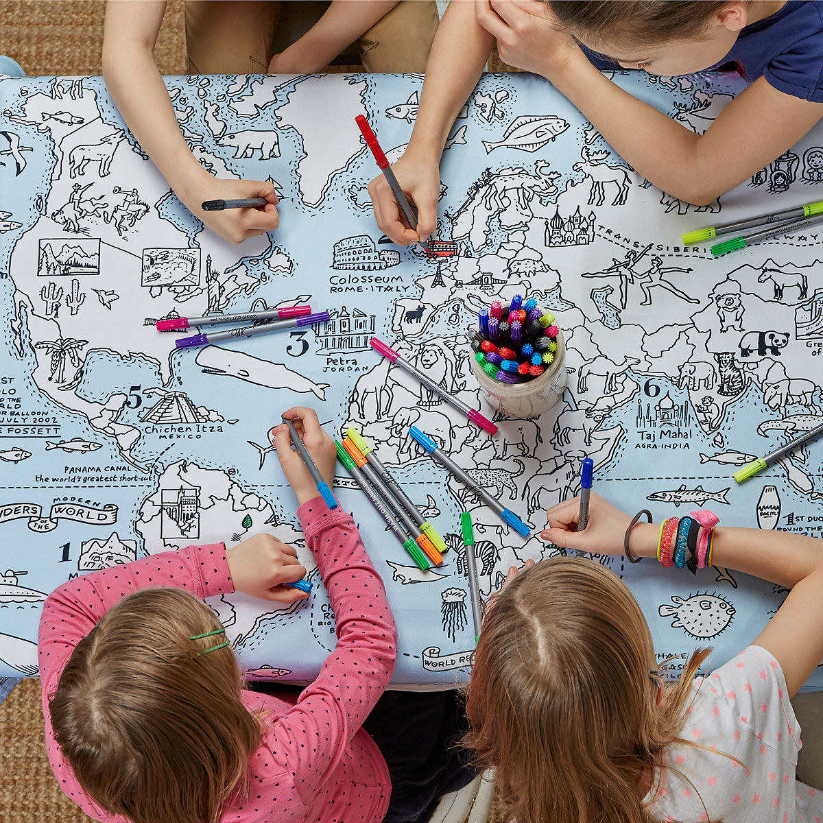 Children color on the tablecloth. It&#x27;s light blue with white, uncolored countries and various things related to each region 