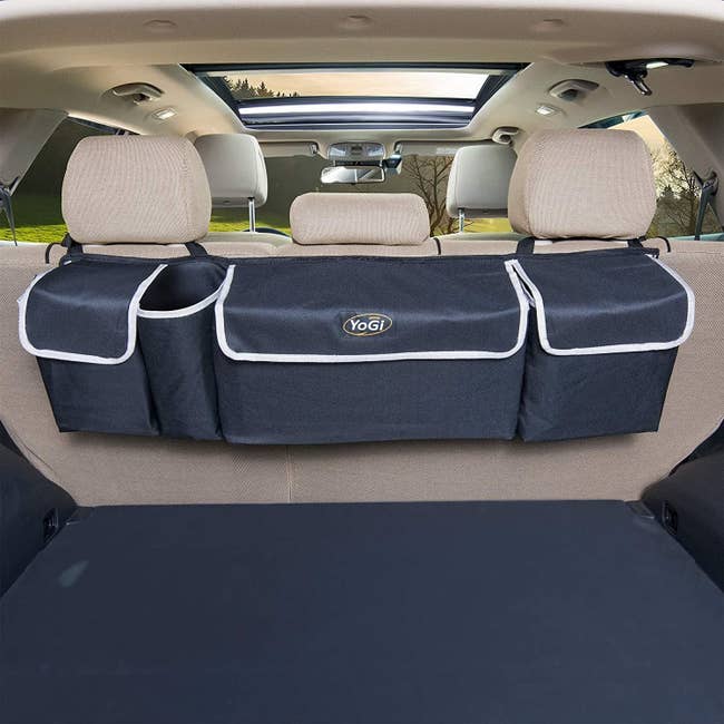 A navy bluish with achromatic piping retention organizer with 3 ample pockets hanging from the backseat into a car's trunk