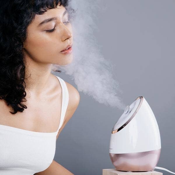 Model with face in front of the steam coming out of plugged in machine