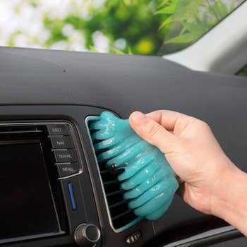 a model's hand using the blue cleaning putty to remove dirt from a car's dashboard air vent