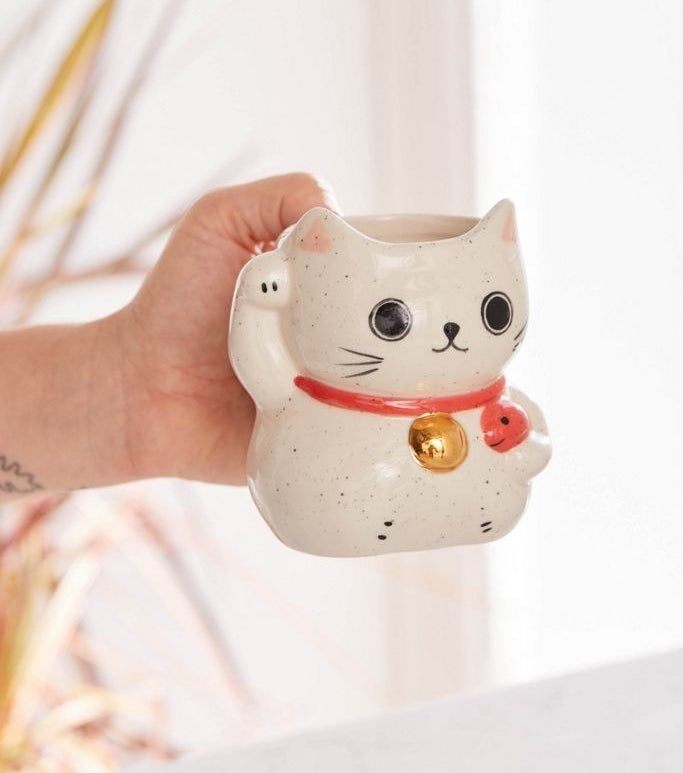 A hand holding up the lucky cat mug 