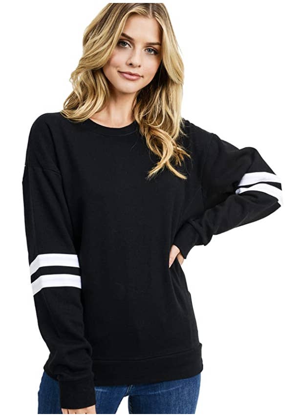 Someone wearing a loose-fitting black sweater with two white stripes around each sleeve 