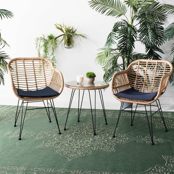 two chairs made of brown rattan with black wire legs and blue seat cushions. matching table with glass top in between the two chairs
