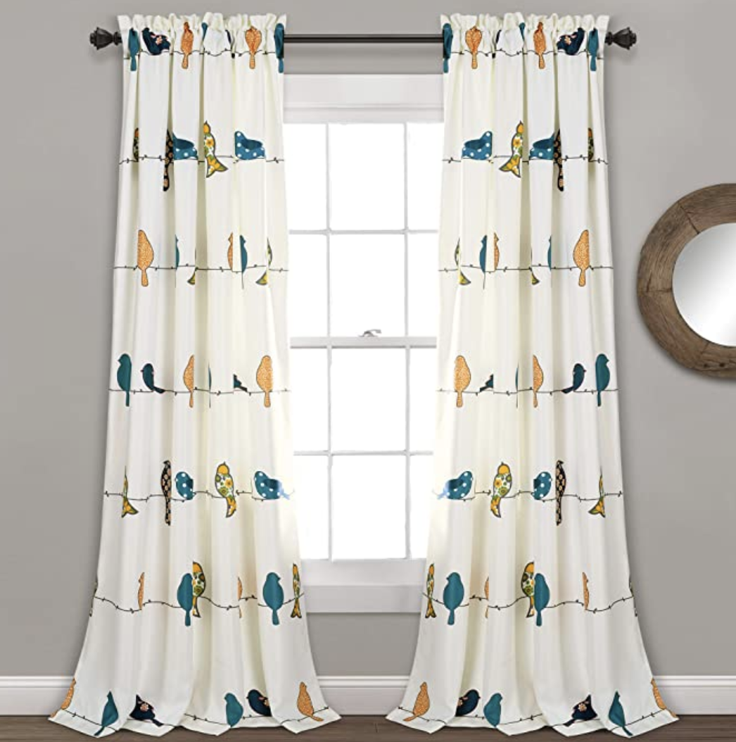 White, flowy window curtains with blue, orange, and black birds as a pattern