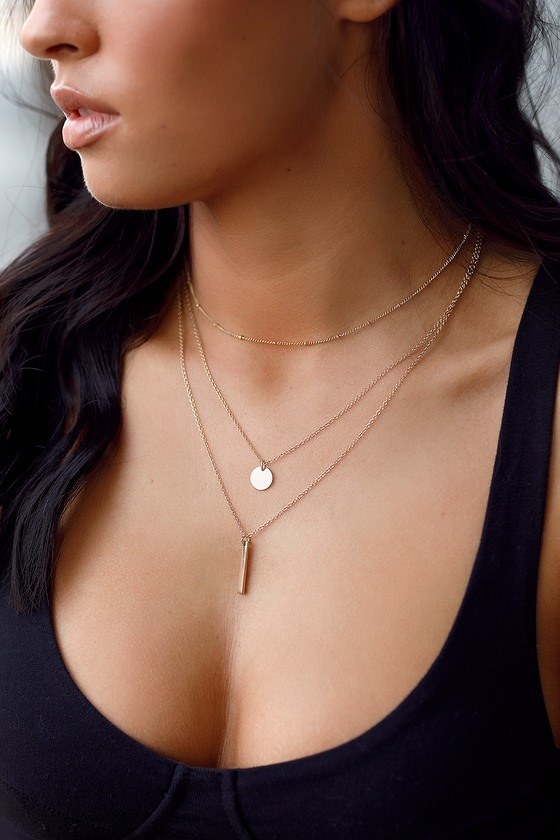 model wearing a gold chain necklace with three layers of different lengths with one round charm and one skinny pendant 