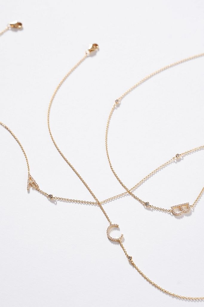 Three separate intertwining gold necklaces with the letters A, B, and C on a white background
