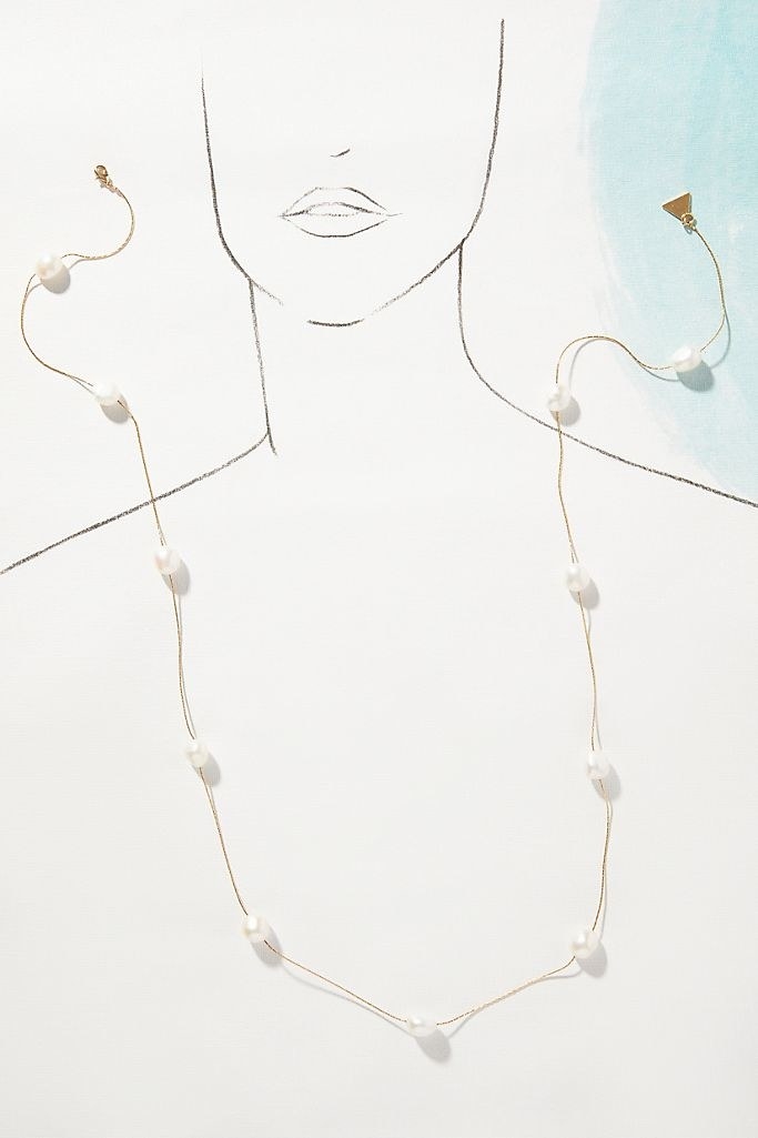 A gold necklace with white pearls spread out around it, laying on top of a sketch of a person's face