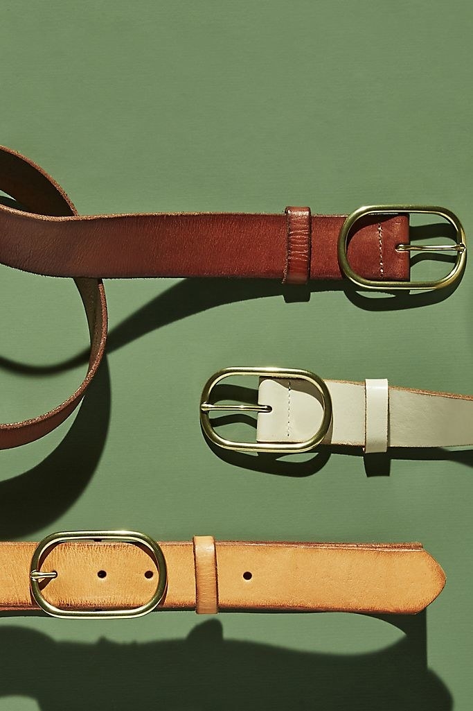 Three leather belts with gold, oval buckles over a solid green background