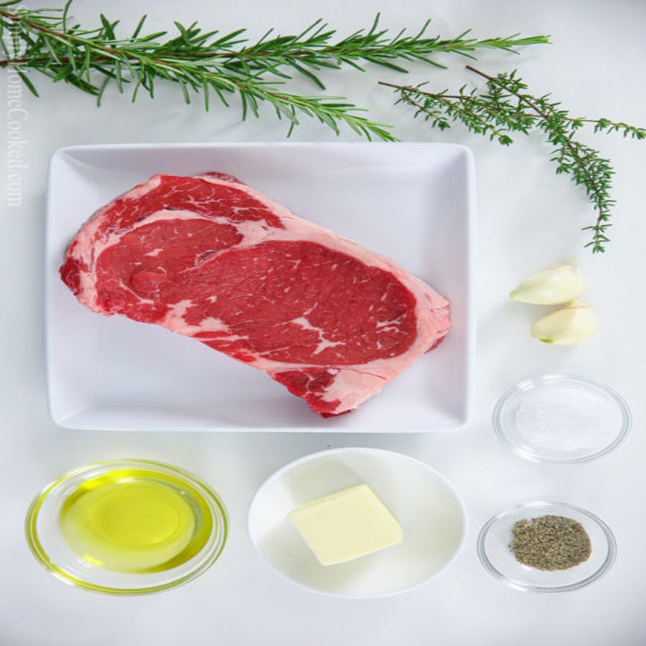Raw steak, oil, butter, garlic, salt, and pepper ready to be cooked.