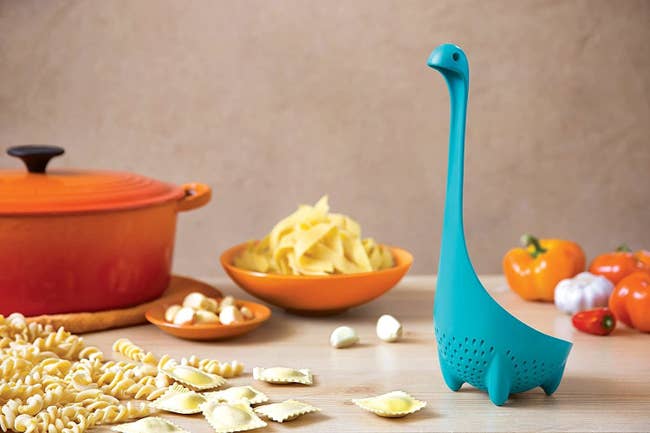 A blue ladle with a long neck and a little head shaped like the Loch Ness monster perched on a table. 