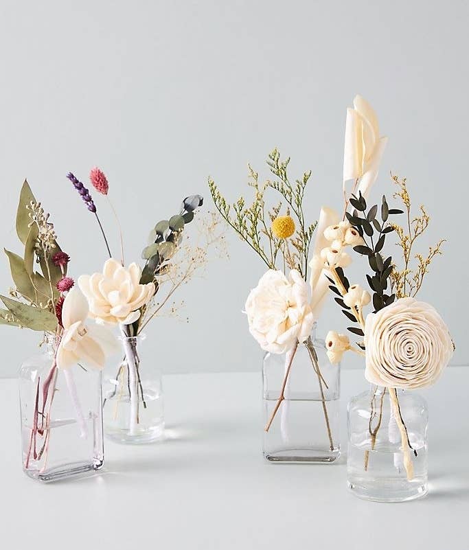 A display of four faux floral diffusers placed in clear jars filled with water 